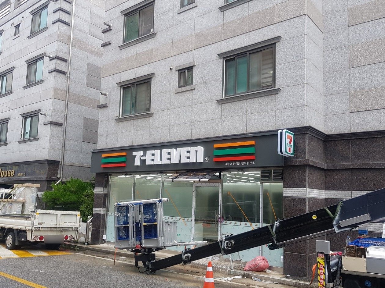 신축 건물 1층의 세븐일레븐 전면 간판과 설치 중인 크레인 장비